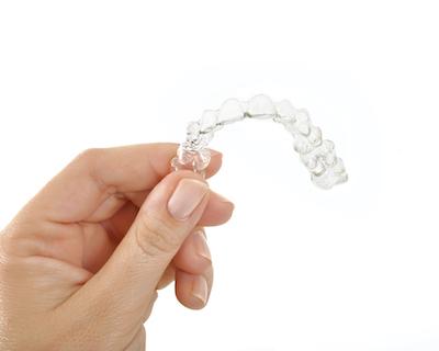Patients hand holding up Invisalign clear aligners tray near 57301